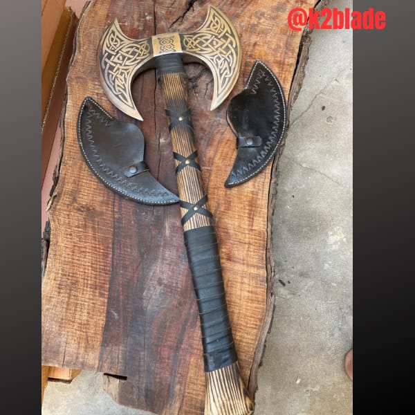 Double bit Viking axe: Matching crescent blades carry intricate knotwork on either side of the handle. A wrapped grip and crossing straps complement the carved wood, with two separate blade covers shown.